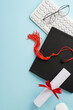 Overhead vertical view of a graduation cap, diploma with red ribbon, glasses, and a white keyboard on a blue background representing online education achievements