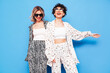 Two young beautiful smiling brunette hipster female in trendy summer costume clothes. Sexy women posing near blue wall in studio. Positive models having fun. Cheerful and happy. In sunglasses