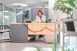 © Oscar - a full view of a young woman sitting at an office desk or clinic reception desk in front of a computer talking on the phone to arrange appointments.