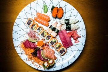 Wall Mural - White plate with assorted sushi rolls on a wooden background