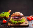 Beef burger with tomato, sauce, lettuce, arugula, cheese, and onion on the wooden board with a dark wooden background