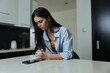 Woman sitting on kitchen counter in blue shirt, looking at phone, casual lifestyle concept