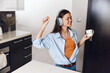 Young woman enjoying a morning coffee in the kitchen while listening to music on headphones