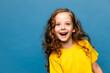 Close-up portrait of cheerful curly hair little girl in yellow t-shirt isolated over vibrant blue color background. Happy children emotion. Copy space for ad, promotion, kids good