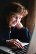 Senior woman typing on a laptop keyboard.