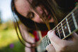 A girl playing the guitar, with the focus on the chords and strings, her face softly blurred in the background.