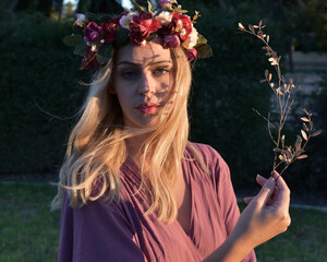 Canvas Print - close up portrait of pretty blonde female model wearing a flower crown wreath and purple dress.  green nature  plants and trees in background