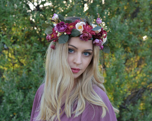 Canvas Print - close up portrait of pretty blonde female model wearing a flower crown wreath and purple dress.  green nature  plants and trees in background