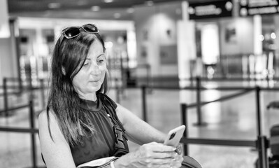 Wall Mural - Portrait of a female tourist looking at her smartphone at the airport. People and lifestyles concept. Travel and Happy life of single woman theme