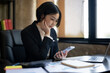 © Wasana - A woman in a business suit is looking at her cell phone while sitting at a desk