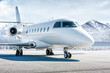 White luxury business jet on airport apron in winter on the background of high scenic snow capped mountains