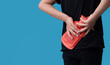 Woman using hot water bottle to relieve back pain on light blue background
