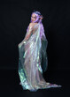 Full length portrait of beautiful female model with long purple hair wearing elf ears, a fantasy fairy crown and  rainbow glitter sequin ball gown.  walking away, back view, isolated dark studio 