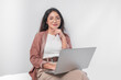 © Reezky - Thoughtful young Asian business woman sitting down with a laptop thinking about work, isolated by white background.