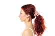 Profile of a young serious woman without makeup tying her long red wavy hair on a white studio background