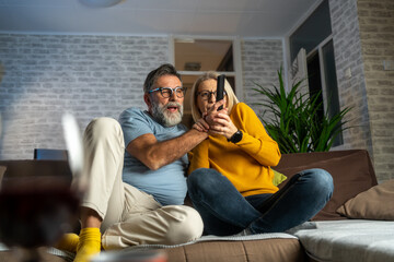 Poster - Cheerful mature beautiful love couple fighting for tv remote while sitting on the sofa in living room. Happy couple sitting on couch at home watching tv