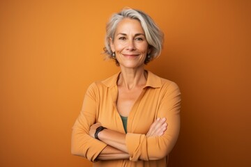 Canvas Print - Portrait of a glad woman in her 50s with arms crossed on pastel orange background
