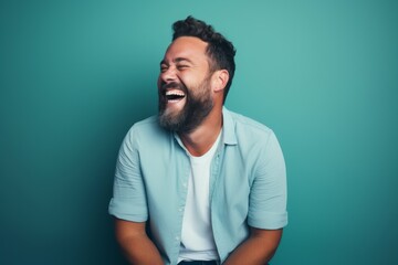 Wall Mural - Portrait of a smiling man in his 30s laughing in front of pastel teal background