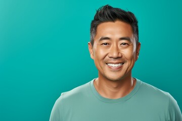 Wall Mural - Portrait of a blissful asian man in his 40s smiling at the camera isolated on pastel teal background
