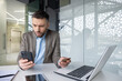 © Liubomir - Businessman shocked by fraud notification while holding credit card and phone in office setting with laptop on desk