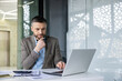© Liubomir - Businessman working thoughtfully on laptop at modern office desk, focusing on a project with concentration.