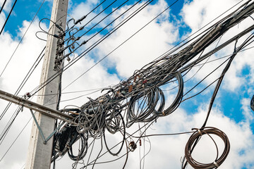 Electric pole and wire with blue sky, wires tangled, cable electricity or telephone line in city of Thailand