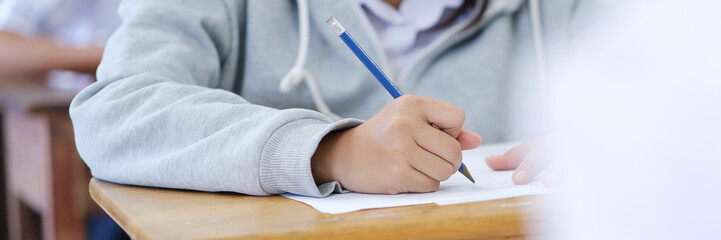 Wall Mural - Close up hand of students reading and taking exam sheets exercises answer with stress in classroom