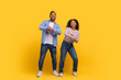 A cheerful African American man and woman stand side by side, dancing and smiling, have fun against a vivid yellow backdrop.