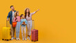 © Prostock-studio - A happy family consisting of a father, mother, son, and daughter stands with their colorful suitcases, prepared to embark on a vacation, pointing at copy space