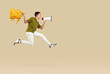 Portrait of a funny happy schoolboy wearing casual clothes holding backpack and mouthpiece jumping on studio beige background. Boy shouting and screaming announcement in megaphone.