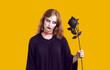 Portrait of mysterious scary dead woman with black rose in her hand on orange background. Witch woman in black dress and with blood on her neck looks at rose with terrible look. Halloween concept.