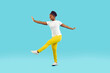 Full body shot of happy funny young African American woman wearing white T shirt and yellow pants pretending to be ballerina and dancing isolated on blue color background