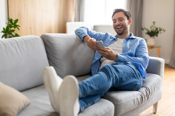 Poster - A man is seated comfortably on a couch, engrossed in his phone. He is scrolling and typing, completely absorbed in the digital device in his hands.