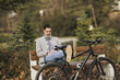 Man Sitting on Bench Next to Bike Using Cell Phone