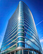 A stunning office tower with a curved glass window facade, set against a clear blue sky. 