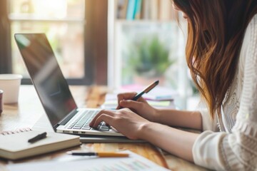 Poster - A woman sitting at a table with a laptop and pen. Suitable for business and technology concepts
