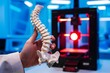 3D printed spinal column model held in hand, red light from printer