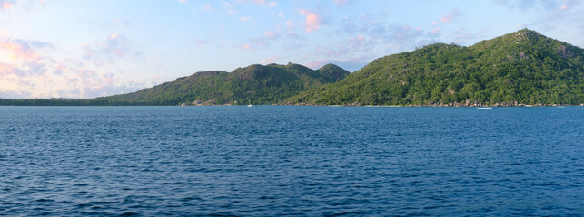 Poster - A beautiful blue ocean with mountains in the background. The water is calm and peaceful. The mountains in the background create a sense of serenity and tranquility
