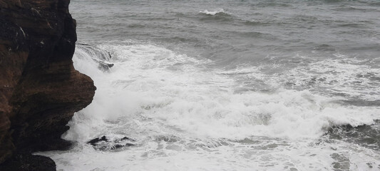 Wall Mural - The waves of the sea are crashing against the rocks on a stormy day.