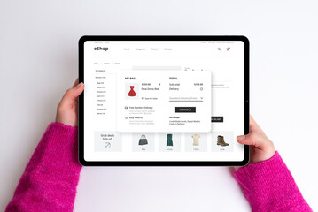 E-commerce cart page on a tablet with price, delivery options, and checkout button. Woman buys a red dress, creating a seamless and stylish online shopping experience