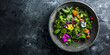 Green fresh mix salad with small flowers in a concrete bowl on a dark gray background. Top view.