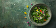 Green fresh mix salad with small flowers in a concrete bowl on a green background. Top view.