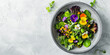 Green fresh mix salad with small flowers in a concrete bowl on a white background. Top view.