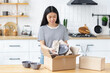 © kucherav - Shopping online or delivery service concept. Happy asian young woman customer at home, opening and unpacking cardboard box carton parcel after buying ordering online