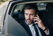 © Nelson - A distinguished, successful senior businessman converses on his mobile phone while seated in his luxurious automobil