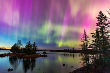 northern lights erupt over a lake in minnesota in a dark sky overhead shining rainbow of aurora ligh