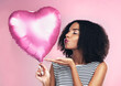 © peopleimages.com - Studio, celebration and girl with ballon in heart shape, blowing kiss and flirting with eyes closed. Female model, anniversary or valentines gift by background, surprise or present for woman