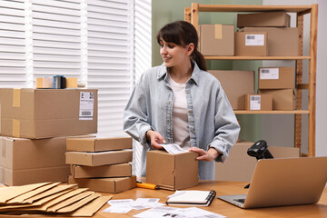 Sticker - Parcel packing. Post office worker sticking barcode on box at wooden table indoors