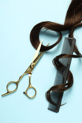 Wall Mural - Professional hairdresser scissors and comb with brown hair strand on light blue background, flat lay