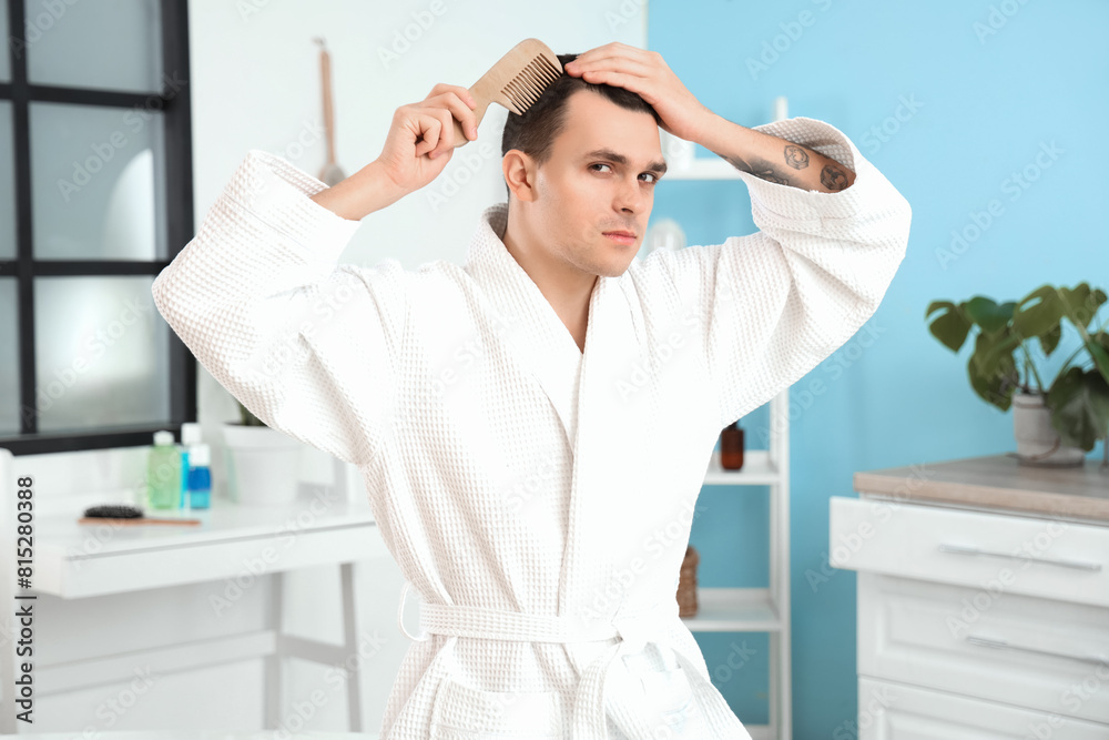 Young man with hair loss problem combing in bathroom